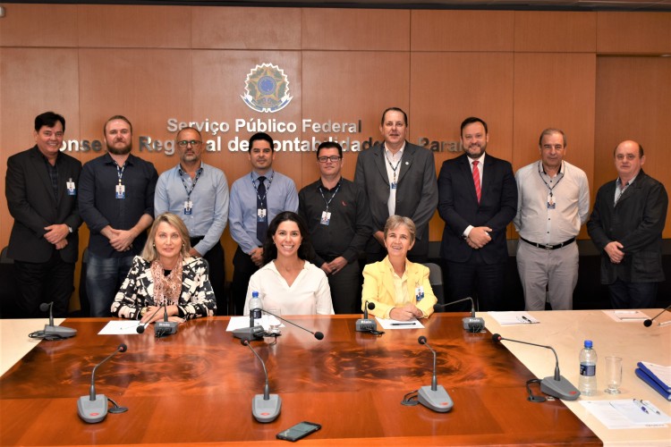 A partir da esquerda, atrás: Hugo Catossi, diretor operacional; Maurício Ostrowski Junior, gerente de Informática; Adilson Fernando Castro, gerente de Registro, Wanderlúcio dos Santos Leite, coordenador da Assessoria Jurídica; Valdair de Souza, coordenador de Contabilidade, Finanças e RH; Gerson Borges de Macedo, diretor superintendente; Roberto Marques de Figeiredo, VP de Adm. e Finanças e coordenador da comissão; Dirceu Zonatto, gerente de Desenvolvimento Profissional; e Aguinaldo Mocelin, VP de Desenvolvimento Profissional. Sentadas: Cristina Medeiros Dias, coordenadora da Secretaria da Presidência; Jeruza Moura Burges, coordenadora de Governança, Riscos, Compliance e Qualidade; e Celita Paltanin, Gerente de Fiscalização.